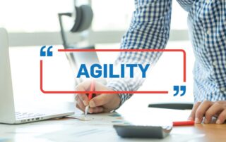 Hände arbeiten am Schreibtisch mit Laptop, eingeblendet das Wort Agility